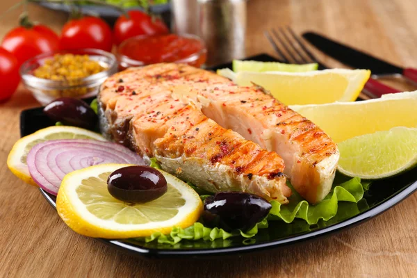 Sabroso salmón a la parrilla con limón y verduras, sobre mesa de madera — Foto de Stock