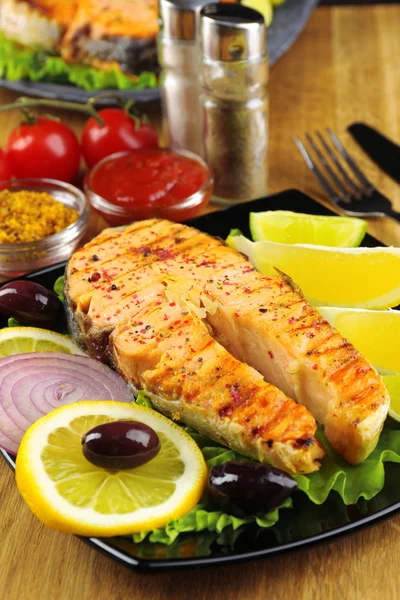 Tasty grilled salmon with lemon and vegetables, on wooden table — Stock Photo, Image