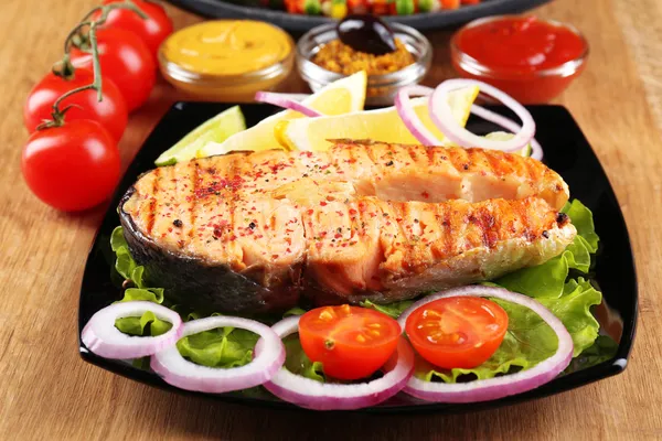 Вкусный лосось на гриле с лимоном и овощами, на деревянном столе — стоковое фото