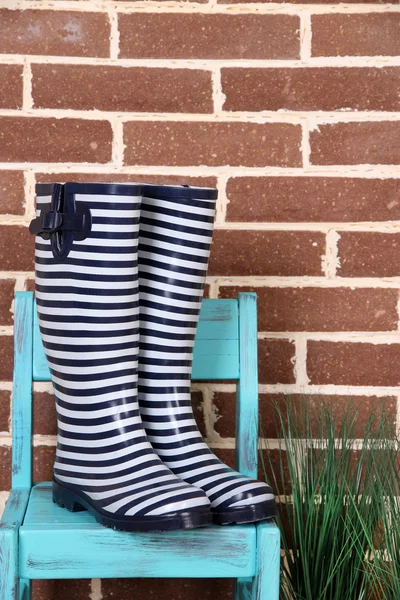 Paar bunte Gummistiefel auf Stuhl auf Farbwandhintergrund — Stockfoto