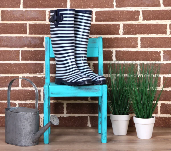 Paar bunte Gummistiefel, Pflanze im Topf, Stuhl und Gießkanne auf farbigem Wandhintergrund — Stockfoto