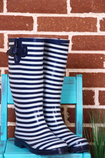 Paar van kleurrijke gumboots op stoel op kleur muur achtergrond — Stockfoto