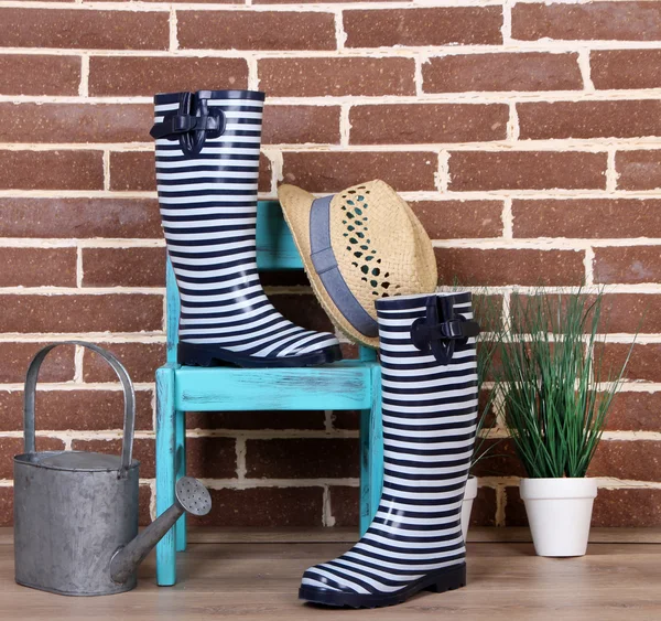 植物の鍋、椅子、壁の背景の色に水まき缶でカラフルなゴム長靴のペア — ストック写真