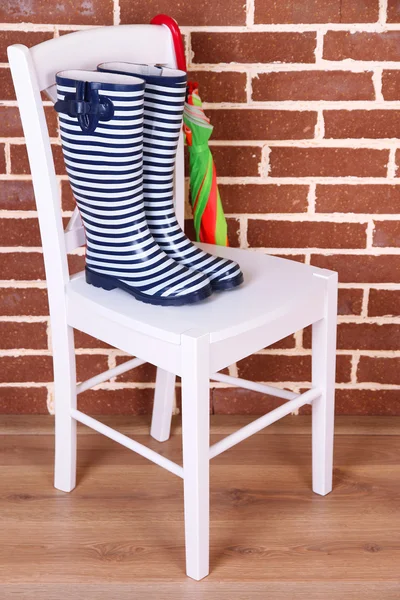 Paire de bottes de gomme colorées sur chaise sur fond de mur de couleur — Photo