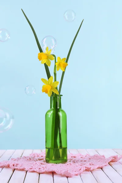 Beautiful irises and daffodils in bottle, on blue background — Stock Photo, Image