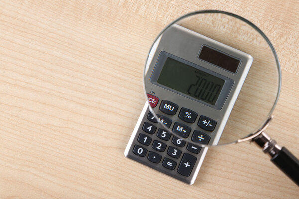 Fraud concept with magnifier and calculator, on wooden background