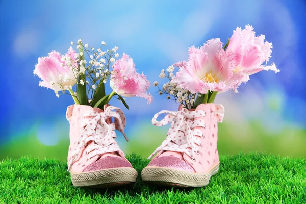 Beautiful gumshoes with flowers inside on green grass, on bright background — Stock Photo, Image