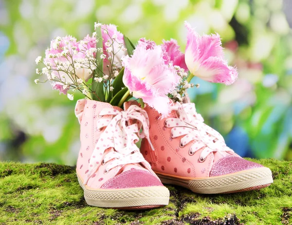 Туфли с цветами внутри на зеленой траве, на ярком фоне — стоковое фото