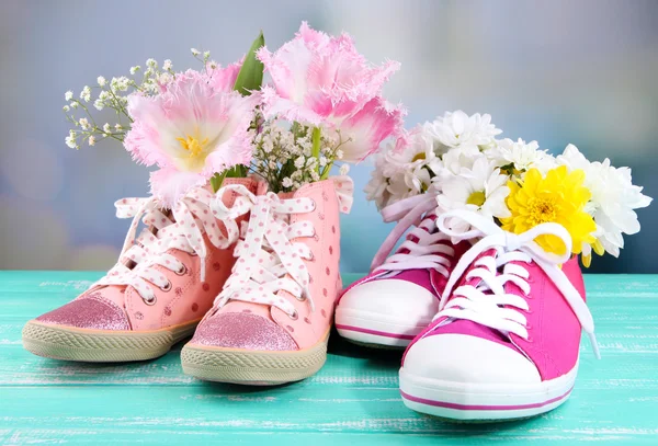 Hermosos zapatos de goma con flores en el interior en la mesa de madera, sobre fondo brillante —  Fotos de Stock