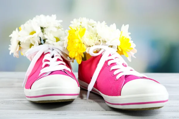 Vackra joggingskor med blommor inne på träbord, på ljus bakgrund — Stockfoto