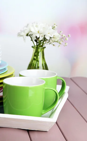 Montón de coloridos platos de cerámica y flores, en bandeja, sobre mesa de madera, sobre fondo claro —  Fotos de Stock
