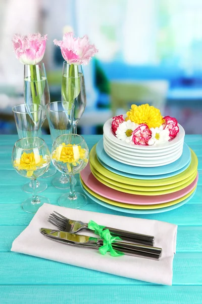 Stack of colorful ceramic dishes and flowers, on wooden table, on light background — Stock Photo, Image