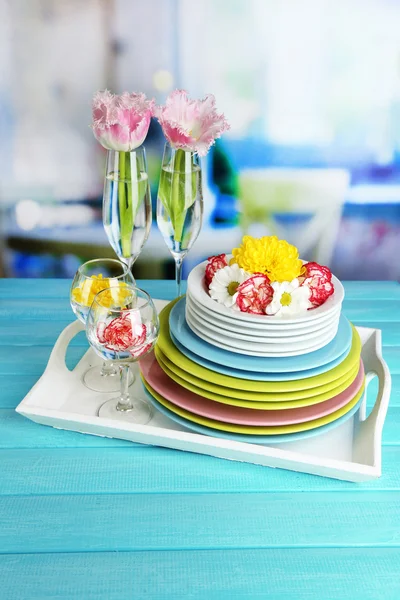 Stack of colorful ceramic dishes and flowers, on tray, on wooden table, on light background — Stock Photo, Image