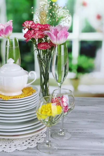 Stack of colorful ceramic dishes and flowers, on wooden table, on light background — Stock Photo, Image