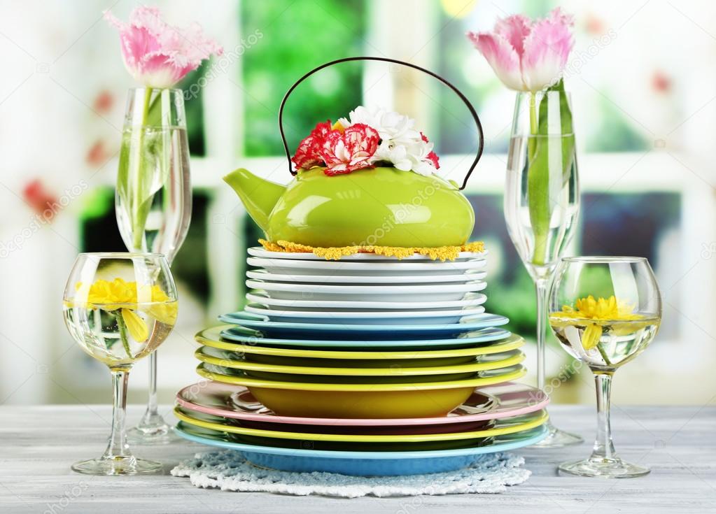 Stack of colorful ceramic dishes and flowers, on wooden table, on light background