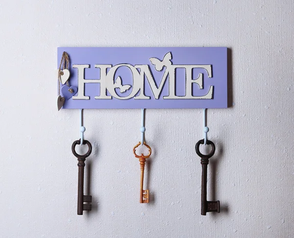 Old keys hanging from hooks, on light wall background — Stock Photo, Image