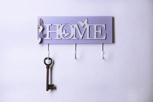 Old key hanging from hook, on light wall background — Stock Photo, Image