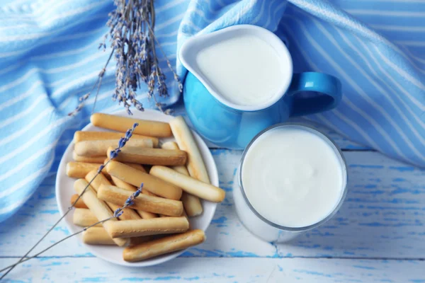 Homemade yogurt in jug and tasty sweet bread sticks on wooden table background — Stock Photo, Image