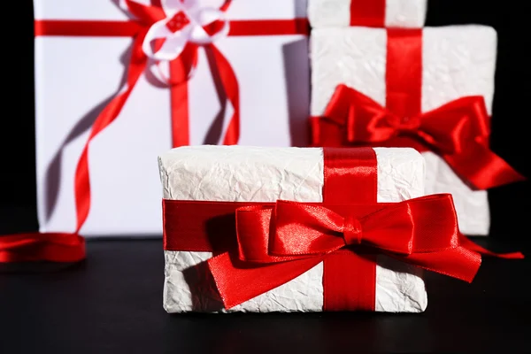 Beautiful gifts with red ribbons, on dark background — Stock Photo, Image