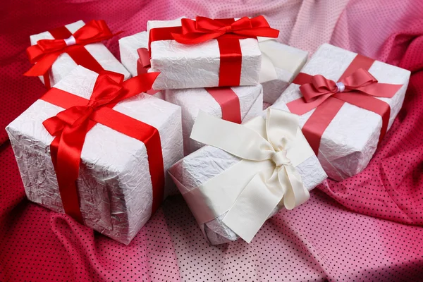 Prachtige geschenken met rode linten op roze doek — Stockfoto