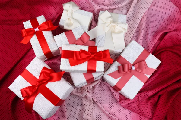 Красивые подарки с красными лентами на розовой ткани — стоковое фото