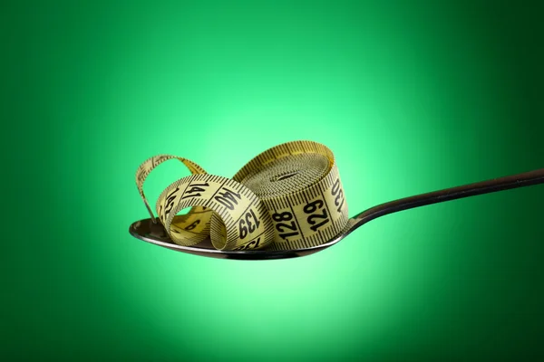 Measuring tape in silver spoon on green background — Stock Photo, Image