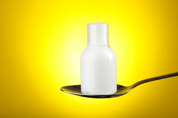 Cosmetic bottle in silver spoon on  yellow background — Stock Photo, Image