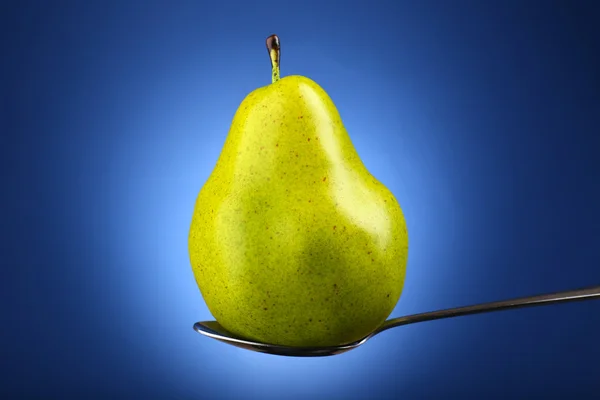 Green pear in silver spoon on blue background — Stock Photo, Image