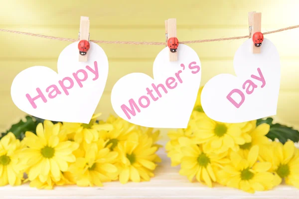 Happy Mothers Day message written on paper hearts with flowers on yellow background — Stock Photo, Image