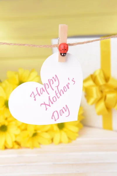 Gelukkig moeders dag bericht geschreven op papier hart met bloemen op gele achtergrond — Stockfoto