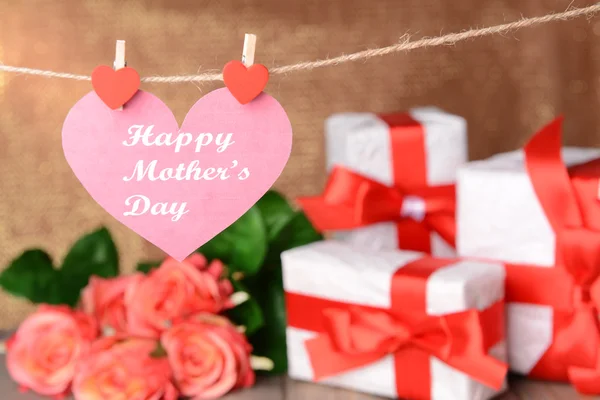 Gelukkig moeders dag bericht geschreven op papier hart met bloemen op bruine achtergrond — Stockfoto