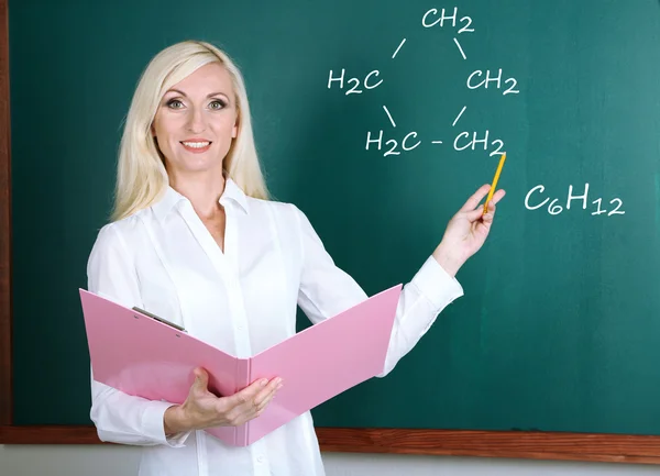 Chemistry teacher explaining formula written on blackboard to her pupils — Stock Photo, Image