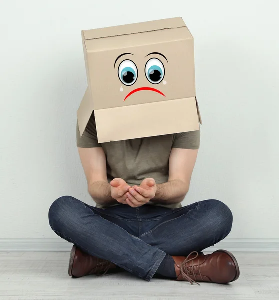 Man with cardboard box on his head sitting on floor near wall — Stock Photo, Image