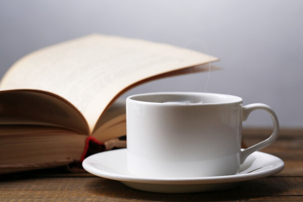 Cup of hot tea with book on table on gray background