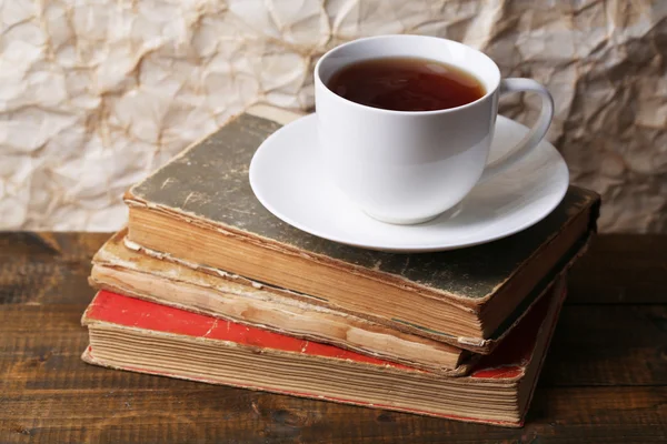 Beker van hete thee op boeken op tafel op papier achtergrond — Stockfoto