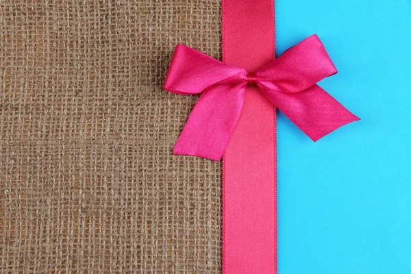 Sackcloth with color ribbon and bow on color paper background — Stock Photo, Image