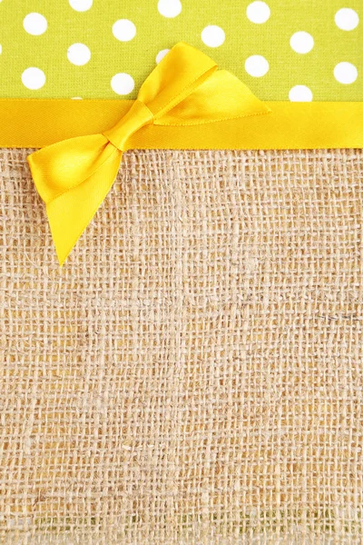 Sackcloth with color ribbon and bow on color fabric background — Stock Photo, Image