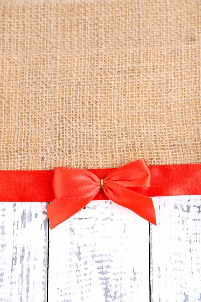Sackcloth with color ribbon and bow on wooden background — Stock Photo, Image