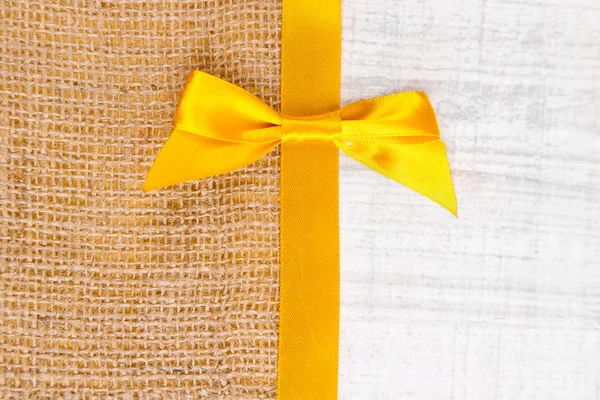 Sackcloth with color ribbon and bow on wooden background — Stock Photo, Image