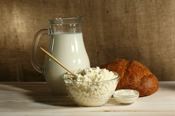 Tasty dairy products on wooden table, on sacking background — Stock Photo, Image