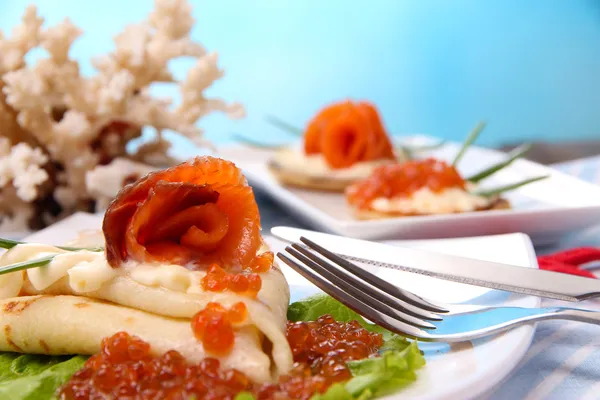 Frittelle con caviale rosso, salmone e maionese, cipolla verde, su piatto, su tovagliolo di colore, su tavolo di legno, su sfondo brillante — Foto Stock