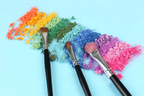 Arco iris triturado sombra de ojos y maquillaje profesional cepillo sobre fondo azul — Foto de Stock