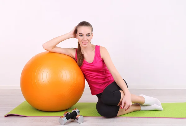 Jovem menina fitness bonita exercitando com bola laranja e halteres no ginásio — Fotografia de Stock