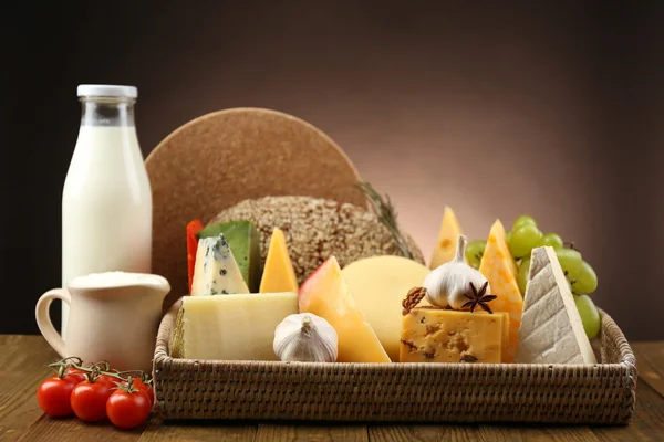Basket with tasty dairy products on wooden tray, on dark background — Stock Photo, Image