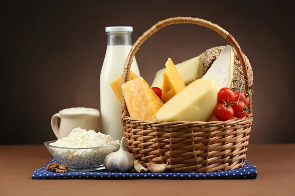 Basket with tasty dairy products on wooden table, on dark brown background — Stock Photo, Image