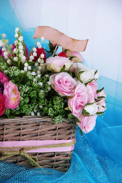 De belles fleurs dans un panier en osier, sur un tissu de couleur et un fond en bois — Photo