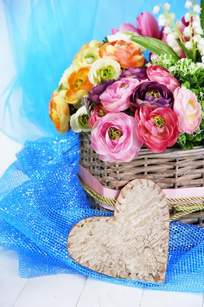 रंगीन कपड़े और लकड़ी की पृष्ठभूमि पर विकर टोकरी में सुंदर फूल — स्टॉक फ़ोटो, इमेज
