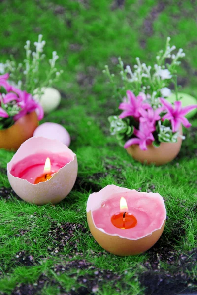 Composizione concettuale pasquale. Candela ardente in uovo e fiori su sfondo verde erba, primo piano — Foto Stock