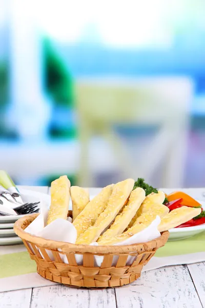 Brotstangen im Weidenkorb auf Holztisch auf hellem Hintergrund — Stockfoto