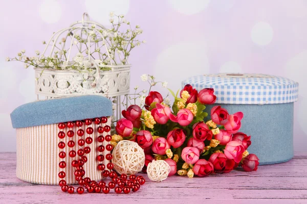 Декоративные коробки с бусами и цветами на столе на ярком фоне — стоковое фото